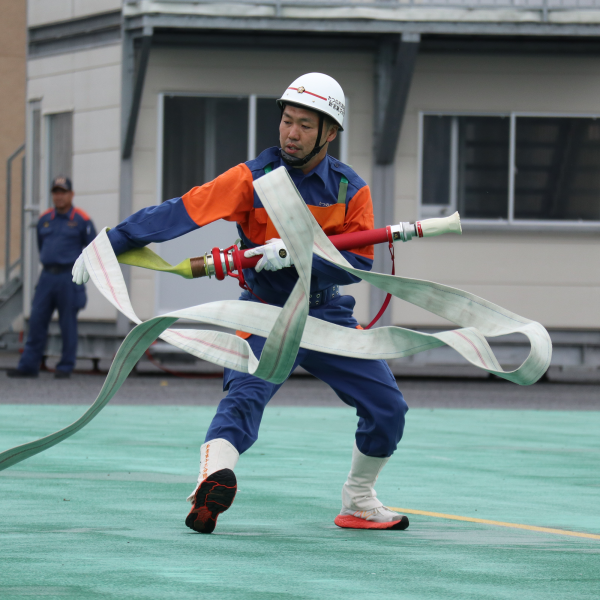 たつの市の消防団員の男性が、放水前の平らで長い消防用ホースを迅速に動かして大会の競技に挑んでいる写真