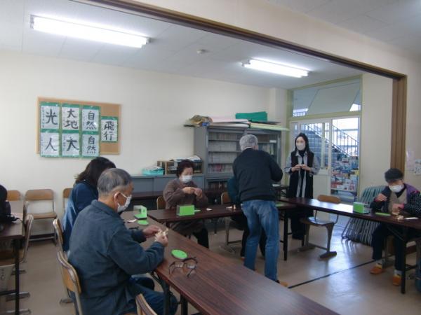 革細工体験教室の参加者たちが、広い部屋に置かれた長机の席に座って革細工を作っている写真
