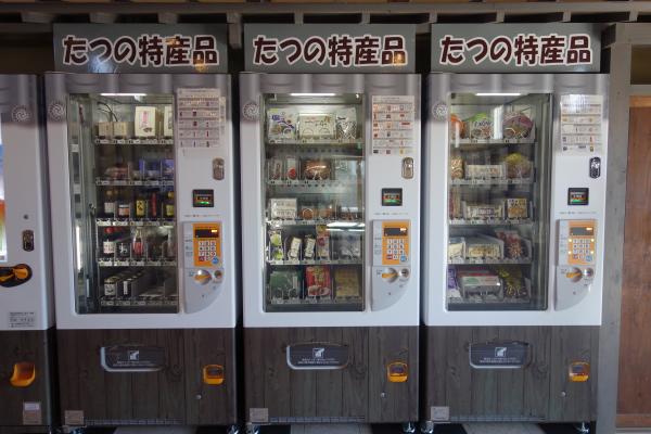 瓶入りの調味料やお素麵などたくさんの種類の特産品が陳列された三台の自動販売機を、正面から写した写真