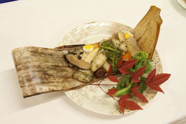 きのこや大ぶりの牡蠣などの具がたくさん入った美味しそうなおこわが、薄い茶色の竹の皮の上に盛り付けられている写真