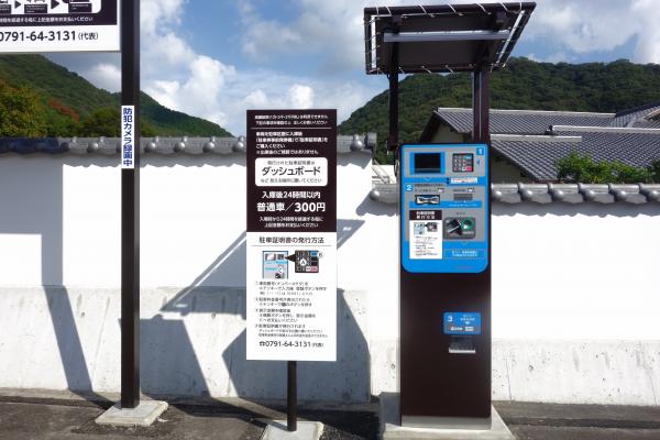 駐車場の料金精算機と、その横に立てられた駐車料金と精算機の案内板を正面から写した写真