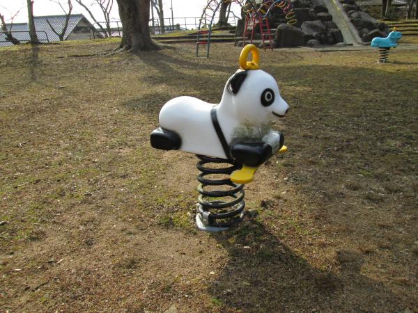 芝生の公園の中にある、白黒のパンダの形をしたスプリング遊具の写真
