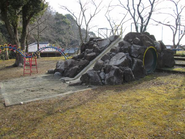 芝生の公園の中にある、石組みの土台の滑り台とその根元にある砂場の写真
