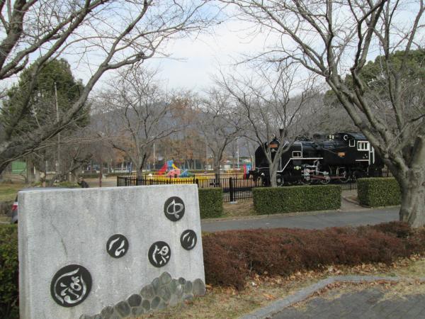 冬の寒空の下、葉の落ちた木々が生え、黒い機関車や遊具の置かれている中川原公園の写真