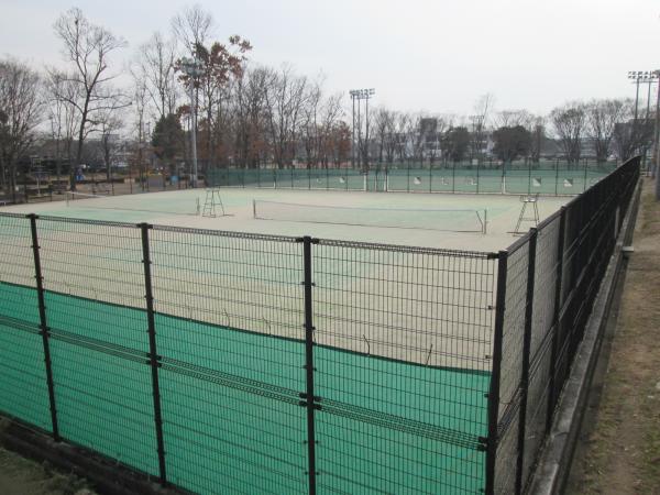 公園内にある黒色の柵で囲われたテニスコートの写真