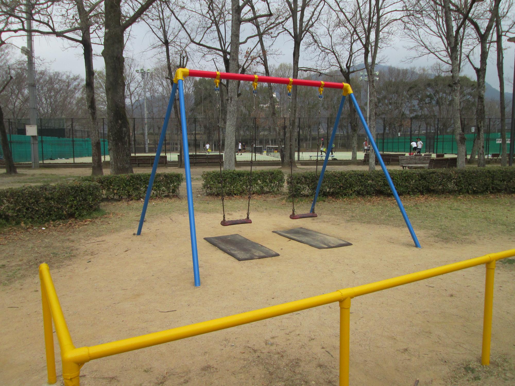 公園の中にある、黄色の柵の中にあるトリコロールカラーのブランコの写真