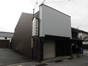 入り口が白、横が茶色の外壁をした建物の写真