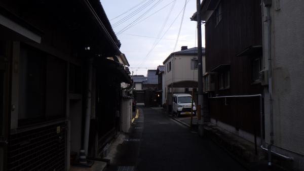 住宅街の薄暗くなってきた狭い路地の左側にタイル張りの家に煙突がある家が建ち並ぶ常照寺垣内の写真