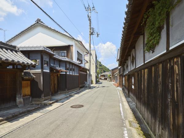 左側に塀に瓦を乗せてある塀瓦と門に瓦を載せた数寄屋門、右側には下が木材、上が白壁の2色の塀で塀瓦が続く紺屋町の写真