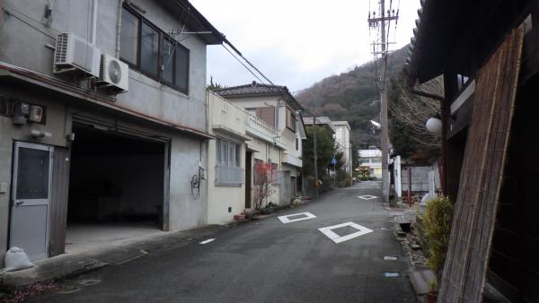 右側には瓦屋根の和風の古民家に玄関には簾が立てかけてあり、左側に2階建ての下がガレージになっているコンクリート建ての家などが並ぶ大手の住宅街の写真
