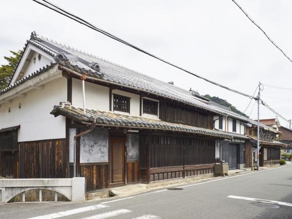 道路の左側には三角屋根に瓦造りの窓には木の格子が設置された歴史を感じる家の外観の写真