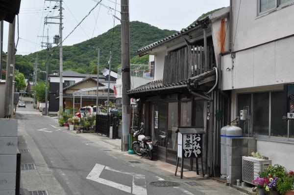 おみやと書かれた看板の後ろに木造作りの歴史を感じる和風造りの2階建ての家などが並ぶ魚町の住宅街の写真