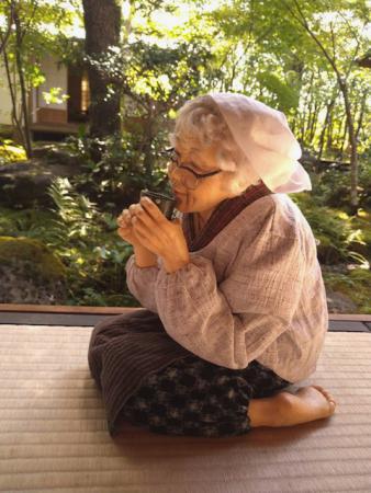 昭和時代のもんぺ姿のお婆さんが縁側に正座してほっこりお茶を飲んでいる人形の写真