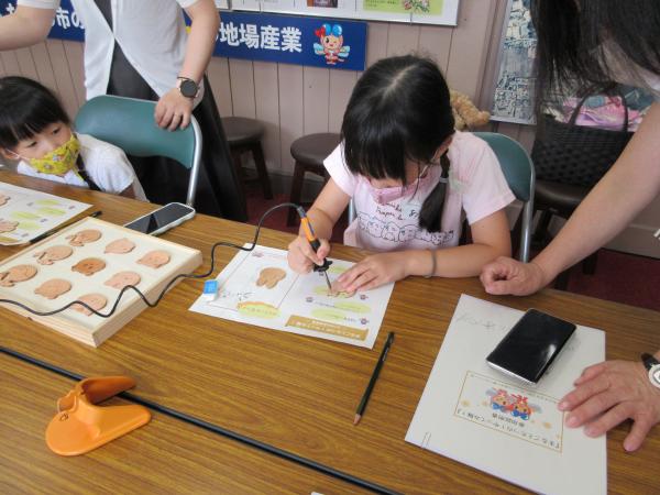 ピンクのシャツを着た女の子が絵付けをしている様子を写した写真