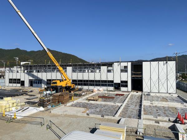 2階建ての仮設校舎の建設現場でクレーンが伸びた工事車両によって工事が進められている現場の写真