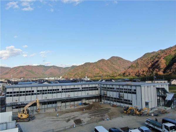 工事が進められているL字型の仮設校舎の前でショベルカーが工事を行っている建設現場の様子の写真