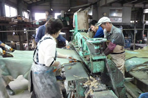4人で皮を機械で押さえ、はさみで切っている写真