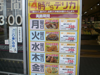店内入り口ドアに、「4時からデリカ」と書かれた曜日ごとのお買い得商品の写真と金額が書かれたポスター写真