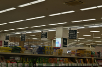 商品棚の間に天井から吊り下げられた深緑の背景に白字で商品名が4つ書かれた看板の写真