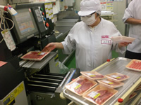 トレイにパックされた肉を手に持った従業員が機械の上に置いている写真