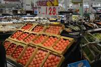 段ボールに敷き詰められたトマトを斜めになった商品棚に複数並べ「安い値」の文字と値段が記載されているポップが立てられている写真