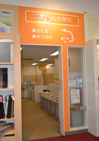 オレンジ色地に白文字で「赤ちゃん休憩室」と書かれた入り口近くに、おむつ替え用のベッドが設置された写真