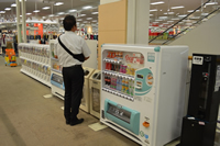 エスカレーター傍の小さな自動販売機の傍で、赤ちゃんを抱っこした父親が立っている後ろ姿の写真