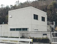 小高い山の麓のフェンスで囲まれた敷地内に、白壁の建物が設置された佐方加圧所の写真