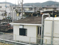 住宅地に囲まれた敷地内に、銀色や白色のタンクに白壁の小さな建物が設置された野田南水源地の写真