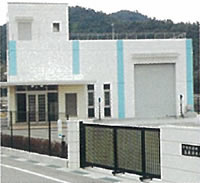 黒いフェンスに囲まれた敷地内に、水色の縦のラインが施された白壁の市場水源地を門の外から撮影した写真
