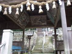 天井の四方に絵のようなものが掛けられている、しめ縄の掛けられている神社の参拝場所に繋がる階段前の休憩小屋のような場所の写真