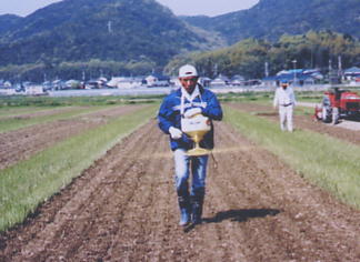 男性が噴霧器を使って畑に除草剤を散布している写真
