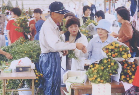 紙で包装した紅花の切花を持った女性と男性が話をしている写真