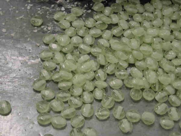金属のテーブルのような場所の上に積まれている、出来上がったばかりの薄緑色の飴の写真