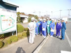 敷地内の案内看板が立つ傍で、ヘルメットを被り作業服を着た男性の話を、紫や青色のジャージ姿の生徒たちが熱心に聞いている写真
