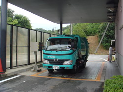 エメラルドグリーン色のトラックが停車した左側に機械が設置された計量機の写真