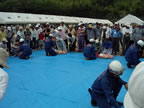 校庭にビニールシートが敷かれ、間隔をあけて置かれたマネキンの傍でヘルメットを被った消防士の方々が片膝をついて座っている訓練の様子の写真