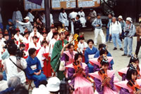神社の境内でそれぞれの衣装を身にまとった女の子たちが奉納を行っている様子を、大勢の観客が見ている小五月祭りの様子の写真