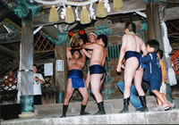 ふんどしに地下足袋姿の男性たちが神社の御社殿で黒い作り物を持ち上げている写真