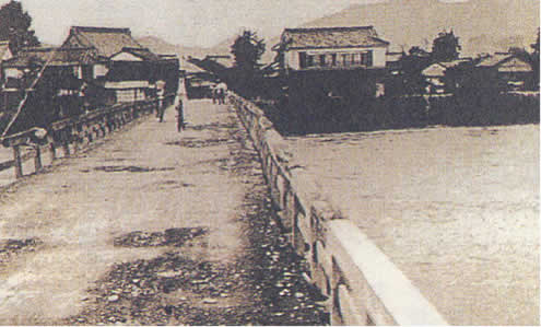 川に大きな木の橋が架かっているモノクロの写真