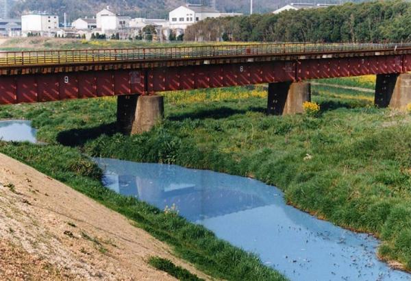 鉄道の高架橋の下をなだらかに流れる川の水の色が水色に濁っている写真