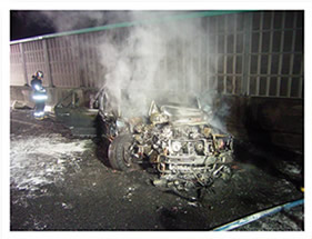 火災を起こした事故車両が、消火活動によって火が消された後に、白い煙のようなものを上げている写真