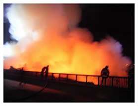 大きな白い煙が上がる火事の現場と、その現場にかけつけた消防隊員の写真