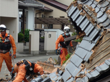 屋根が崩れ落ちている家で3名の消防士が捜索活動をしている写真