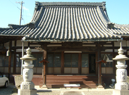 石で作られた灯籠が両側にありその奥に瓦葺屋根のお寺を正面から写した写真