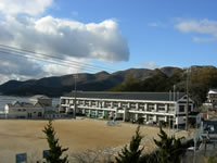 山の麓に建つ2階建ての校舎と校庭を、高台から撮影した室津小学校の写真