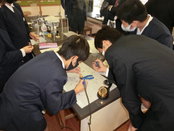 他の生徒が見ている中、1人の生徒が机ではんだづけをしている写真