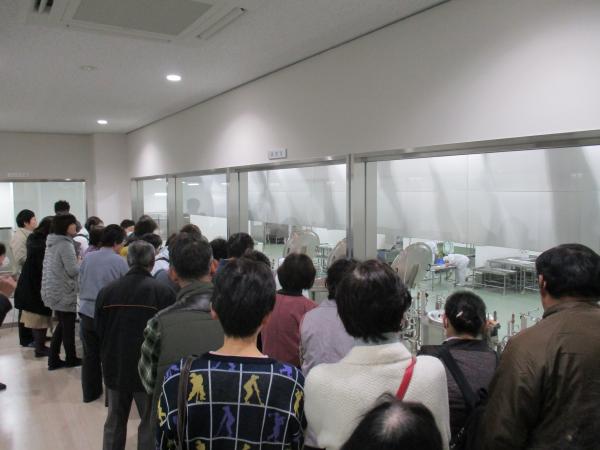大勢の参加者の方が窓ごしに給食センター内を見学している様子の写真