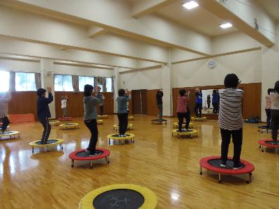 1人用のミニトランポリンが数台並べられており参加者がミニトランポリンの上で両手を上げている前で講師が動きの見本をしているヘルシービクスの写真