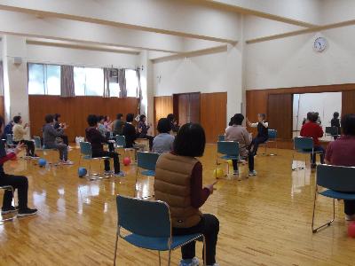 椅子に座り、前にいる講師の動きをに合わせて体を動かしているチェアビクスの写真